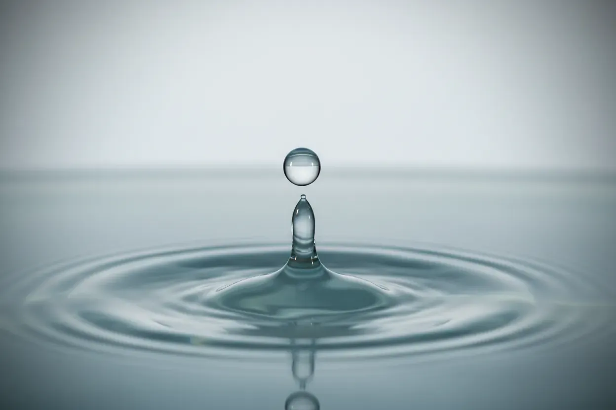 Water droplet creates gentle concentric ripples on a calm surface, symbolizing steady, unobtrusive benefits communication rhythm.